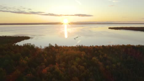 aerial pullback, woods with fall foliage, sunset over large lake in background