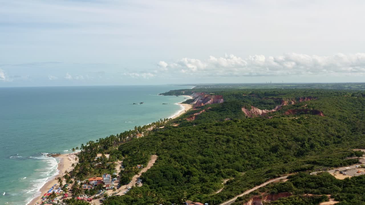 fotografía aérea de la famosa playa tropical de coqueirinhos en paraíba, brasil con paraguas de colores, acantilados cubiertos de plantas exóticas, palmeras, arena dorada y agua turquesa