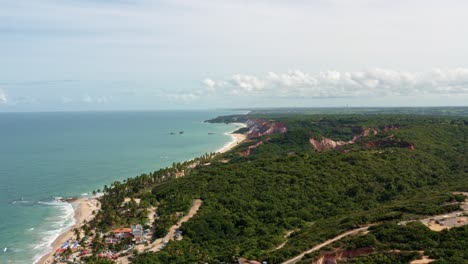 Extreme-wide-aerial-drone-shot-of-the-famous-tropical-Coqueirinhos-beach-in-Paraiba,-Brazil-with-colorful-umbrellas,-cliffs-covered-in-exotic-plants,-palm-trees,-golden-sand-and-turquoise-water