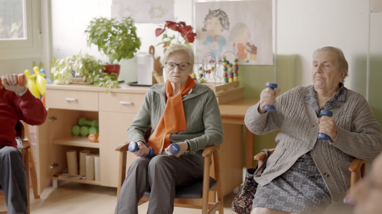 Seniors exercising in a nursing home using pedals and dumbbells