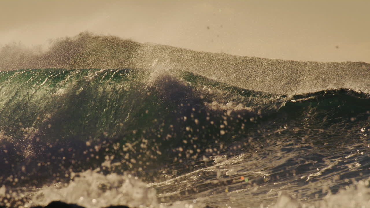 Slow motion view of surfer at golden hour dropping in on set wave as the water crashes against rocky shoreline