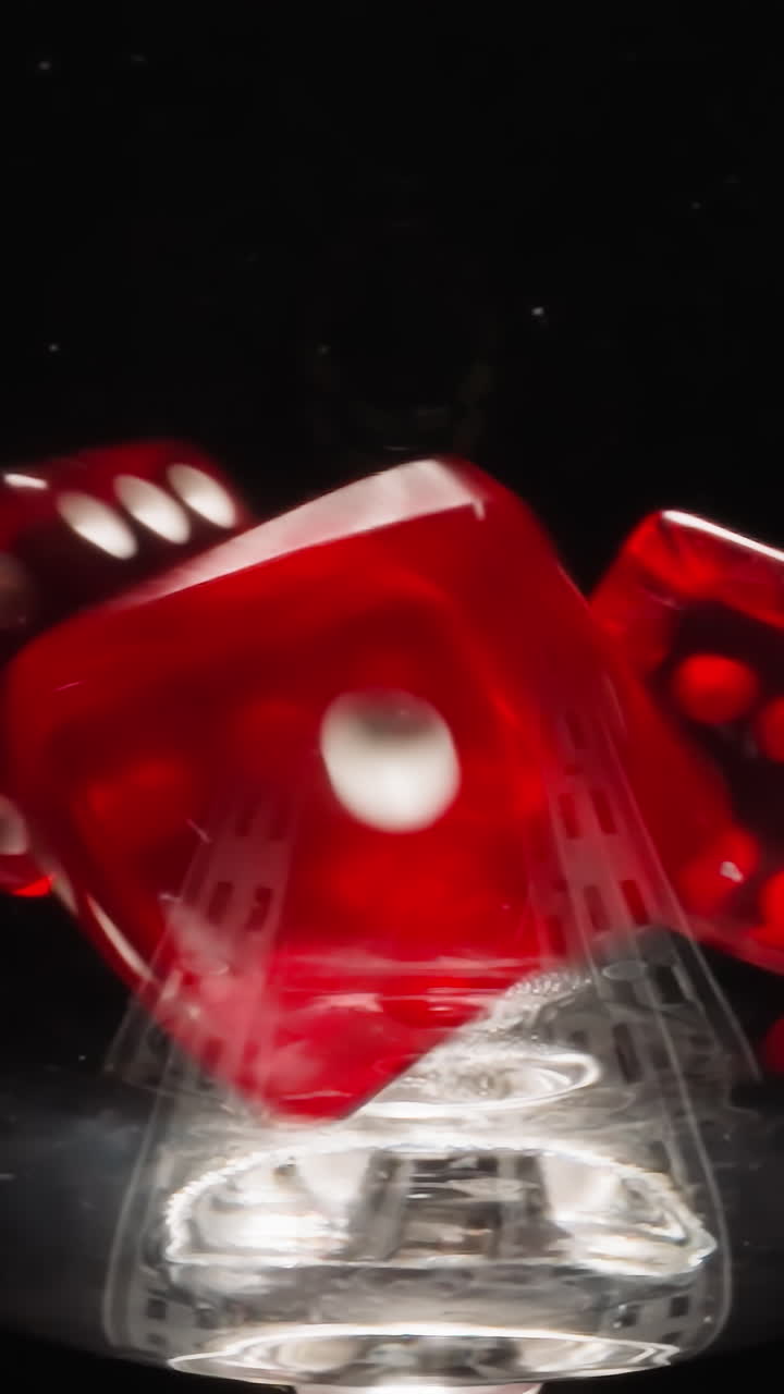 Small red cubes with white dots thrown into transparent glass bounce as dancing and stop on black. Dice for gambling games in glassware at reflecting bright light macro