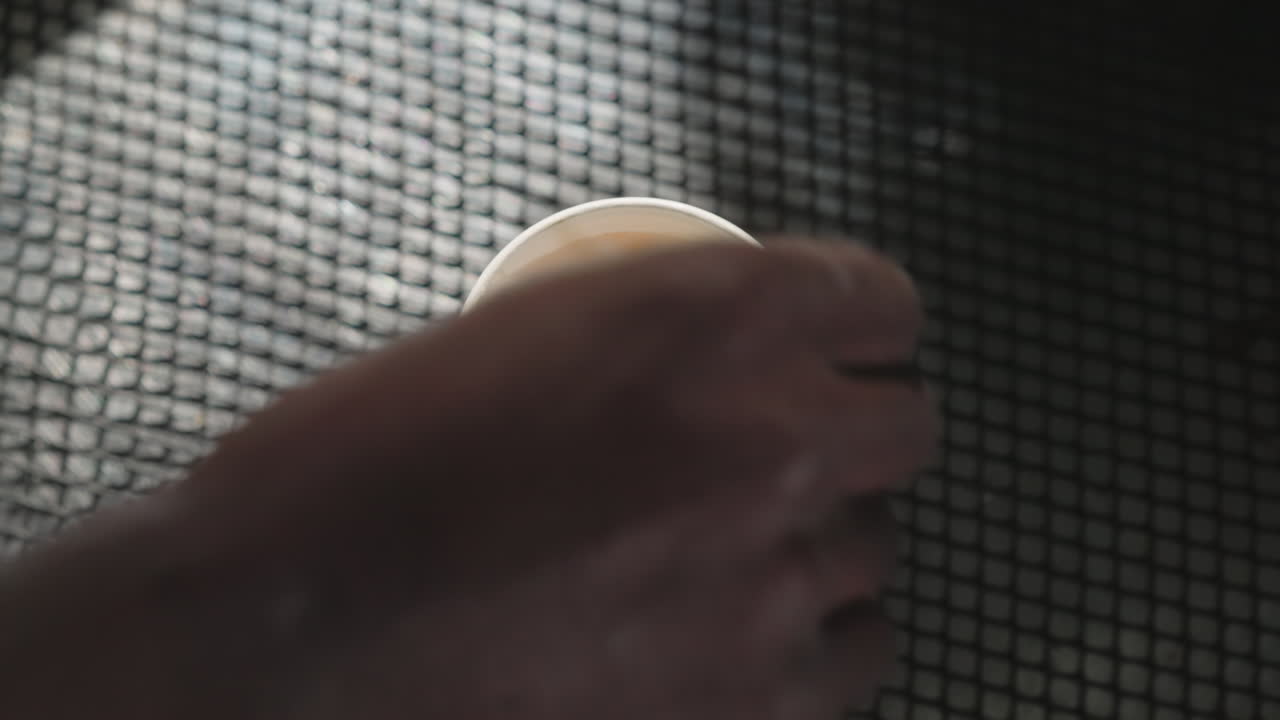 Close-up of a person's hand gently removing a paper filter from a coffee cup, revealing foam inside. The action highlights attention to detail in coffee preparation, with focus on the drink's texture