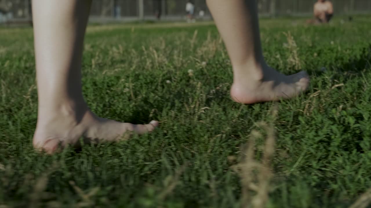 Slow-motion of a barefooted woman walking on the grass in a park in Montreal