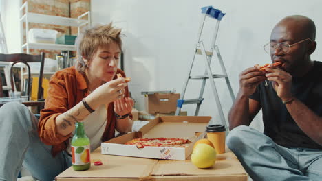 couple eating pizza and having rest in living room under renovation