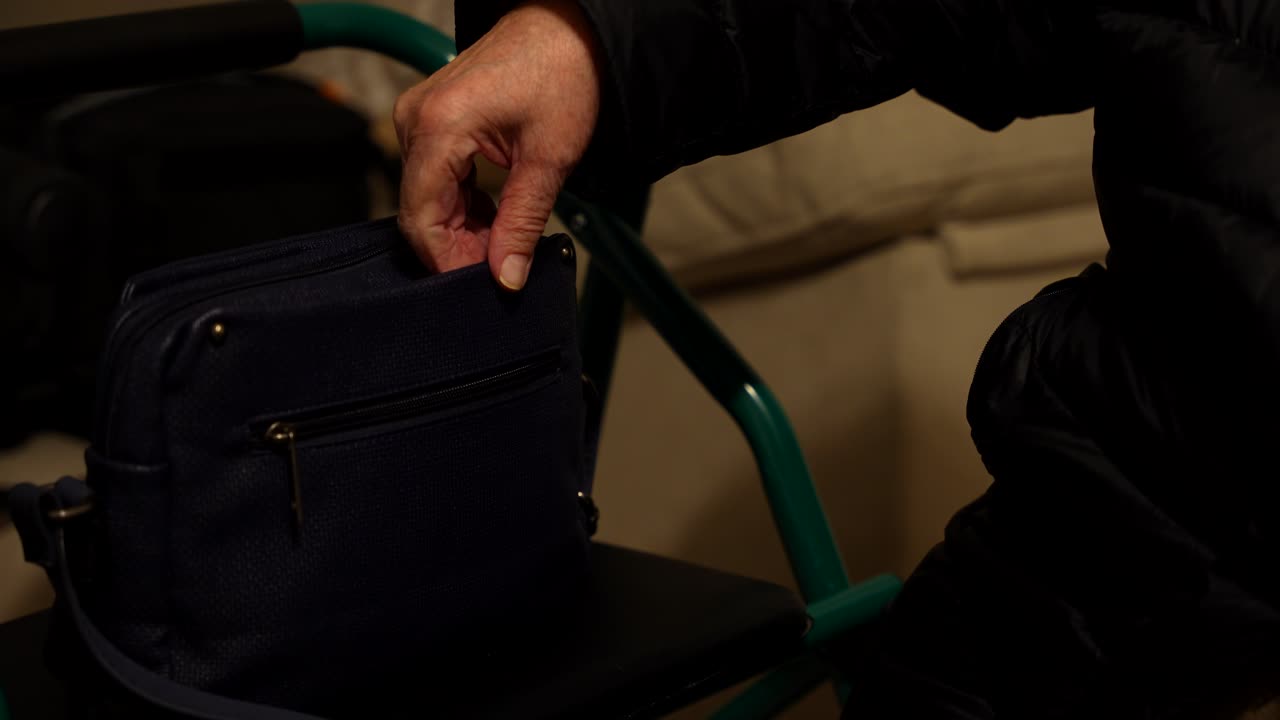 Close-up of elderly woman's wrinkled hand searching handbag beside walker
