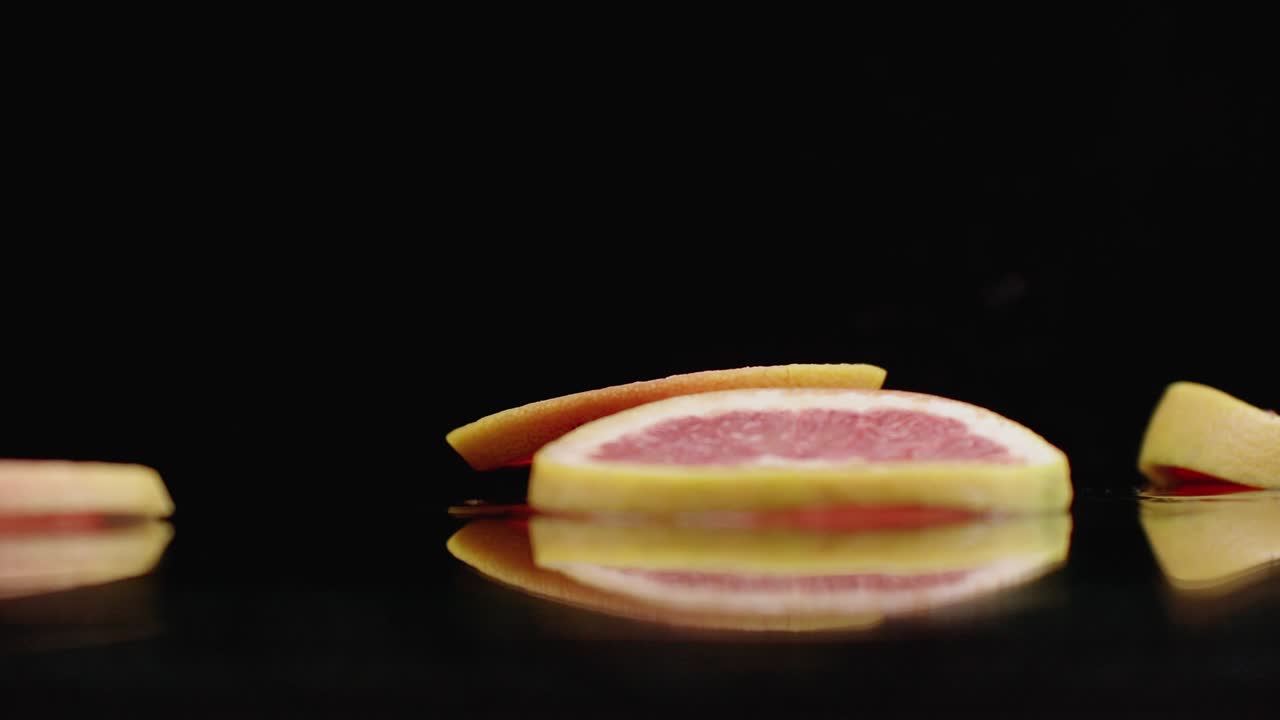 anillos de pomelo en rodajas que caen con salpicaduras de agua en el vaso sobre un fondo oscuro. frutas cítricas jugosas