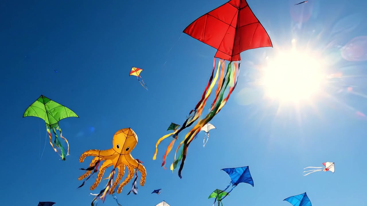 Aquiloni colorati che si librano nel cielo azzurro e luminoso con un impressionante aquilone a forma di polpo che apre la strada sotto il sole radioso.