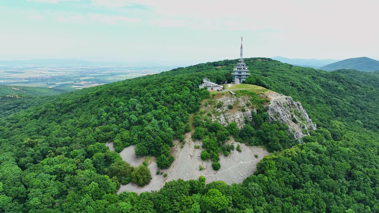 Drone footage of Zobor hill in Nitra, Slovakia, featuring lush forest, rocky slopes, and a tall broadcasting tower on the summit