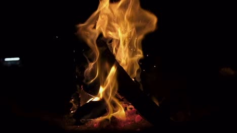 Wide-shot-of-campfire-burning-in-slowmotion,-black-background,-bright-hot-flames-burst-in-sparks