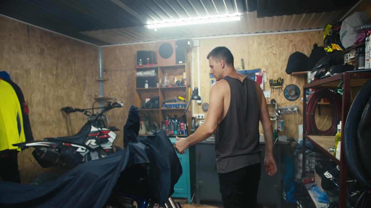 An experienced man mechanic enters his garage workshop and removes the cape from his motorcycle. Start of the working day in the workshop. Starting a new job