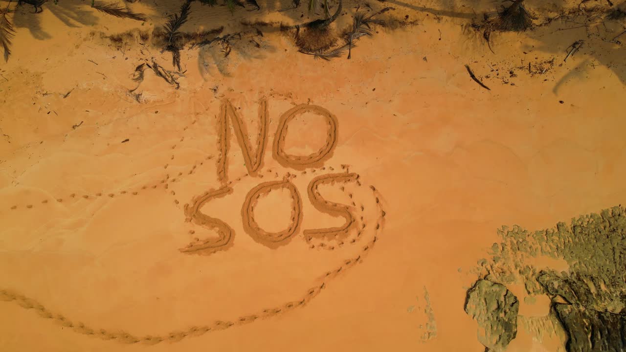 Aerial view of a desert beach with inscription in the sand saying No SOS . Descendig drone shot