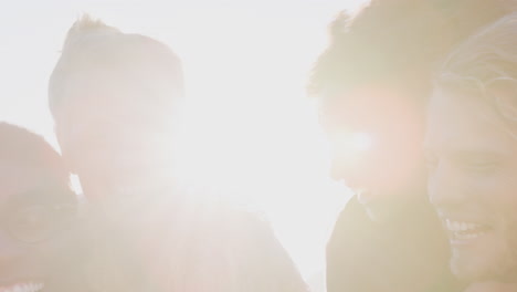 portrait of men giving women piggybacks as group of friends smile against flaring sun