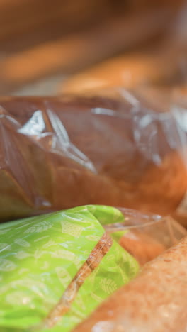 vista de una mano con dos pulseras de cuentas tocando un pan en una tienda de comestibles. disparado con una cámara de mano, capturando la interacción detallada con el pan en la sección de panadería