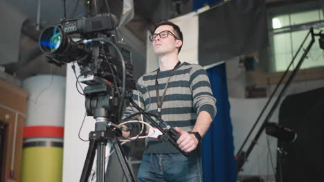 camera operator adjusting equipment in tv studio, focusing on camera while preparing for filming. studio setup with crew member operating high-end broadcast camera on tripod