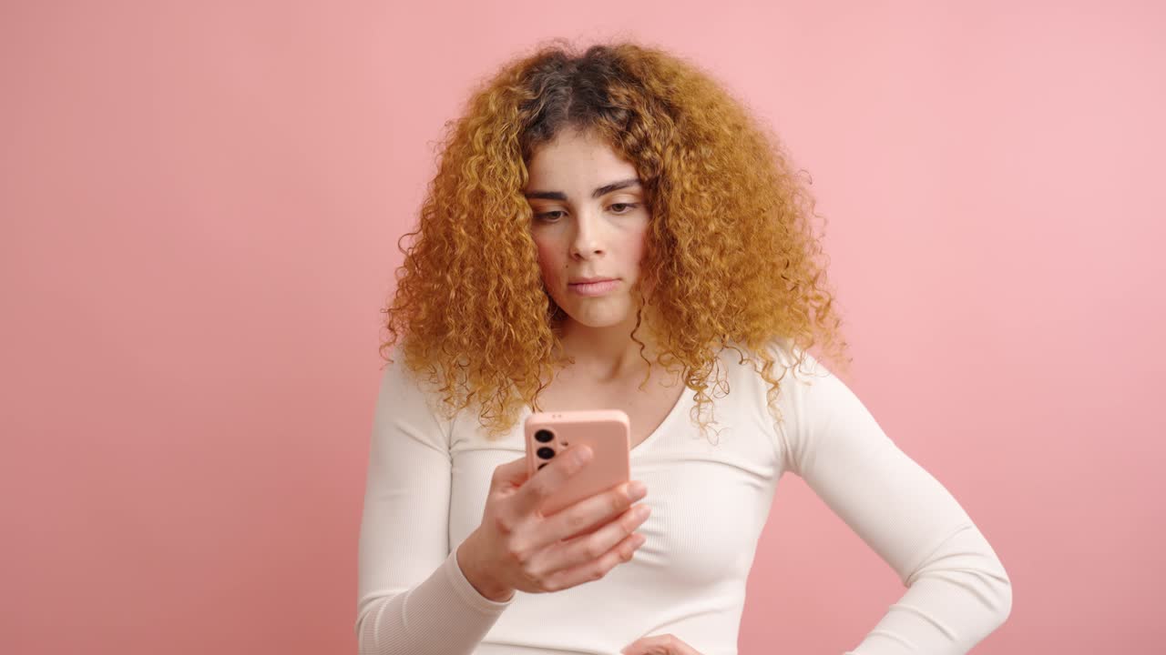 Giovane donna che esprime delusione mentre usa lo smartphone su sfondo rosa