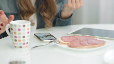 manos de mujer en primer plano usando un teléfono inteligente durante el desayuno en la cocina.