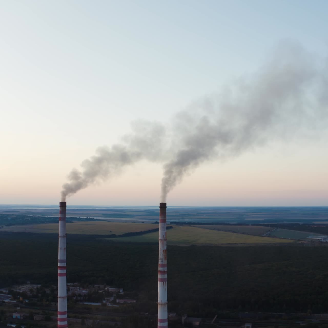 Two pipes with smoke on the beautiful landscape of nature. White smoke pouring out from industrial pipes in the air in the evening.
