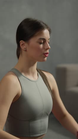 vertical video of a confident brunette girl in a gray swamp doing yoga and breathing practice in a modern apartment at home. a confident athletic brunette girl in a gray swamp is engaged in breathing practices to develop her spiritual peace