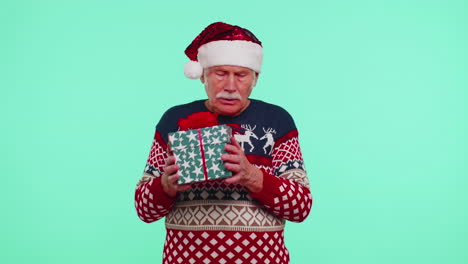 Senior-grandfather-man-in-Christmas-sweater-received-present,-interested-in-what-inside-gift-box