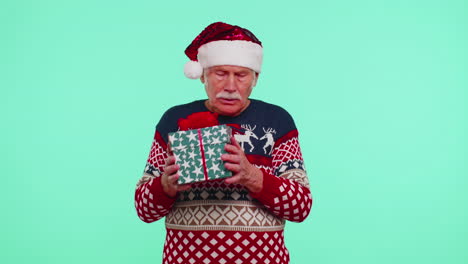 senior grandfather man in christmas sweater received present, interested in what inside gift box