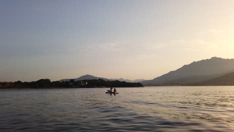 father, daughter and dog sit on a surfboard and paddle on the ocean during sunset