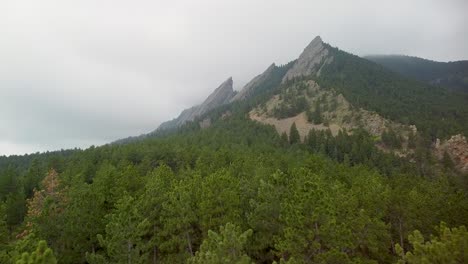 Aerial-ascending-view-over-trees-of-Flatirons-rock-formations,-Boulder,-Colorado