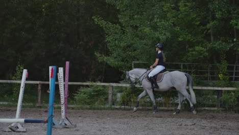 professional girl rider galloping on a horse. girl riding a horse on an arena at sunset. horse hoof creates a lot of dust. competitive rider training jumping.