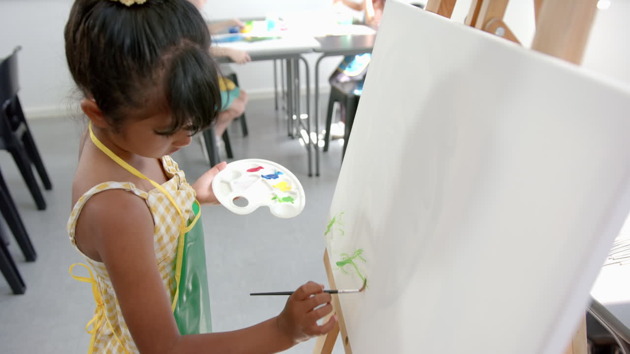 Biracial girl painting on a canvas in a school classroom, focused on her artwork