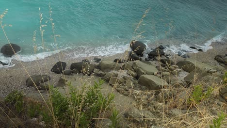 rocky coast in mediterranean with wild grass on hills above turquoise sea, windy summer day