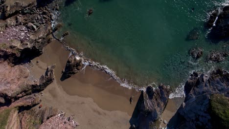 cornwall beach surrounded by rocks and ocean waves from an aerial rotating drone high above the cornish coastline, england, uk