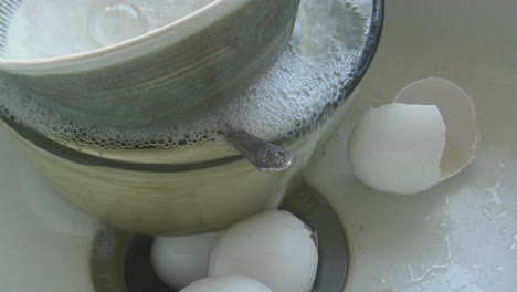 water runs into a sink containing dirty dishes and eggs  shells