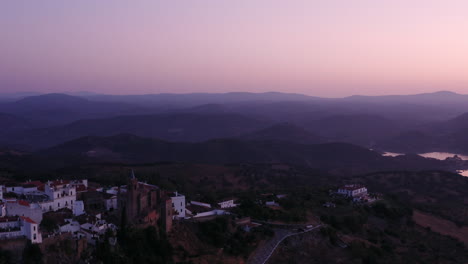 Drone-shot-of-beautiful-cathedral-standing-in-a-Spanish-town,-showing-it's-stunning-river-and-mountain-landscape