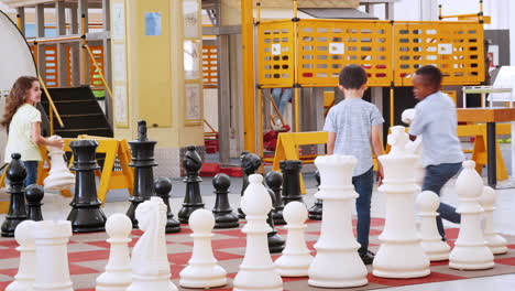 tres niños jugando al ajedrez gigante en un centro de actividades científicas