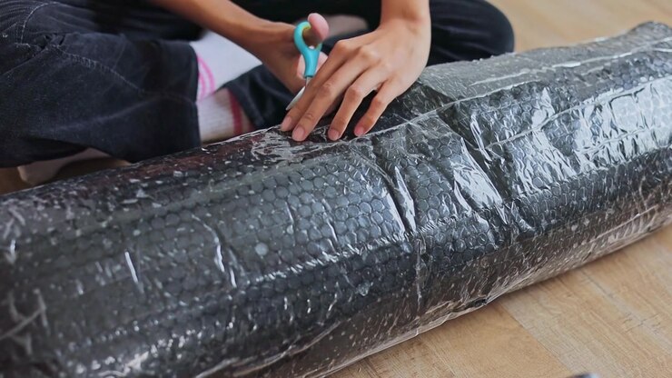 Close-up on hands carefully cutting open plastic bubble wrap packaging with scissors on floor