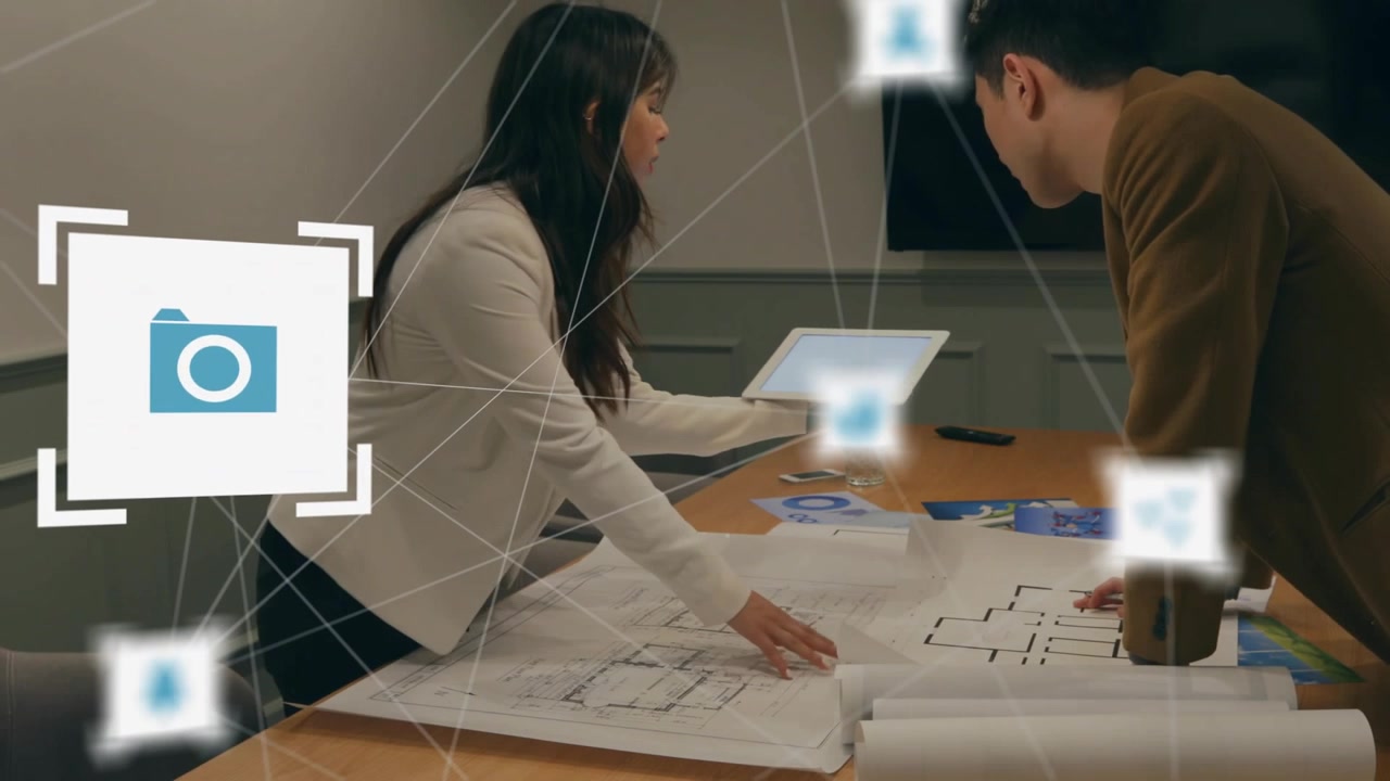 Man leaning over plans while woman placing tablet initiating joint design, AR icons linking points