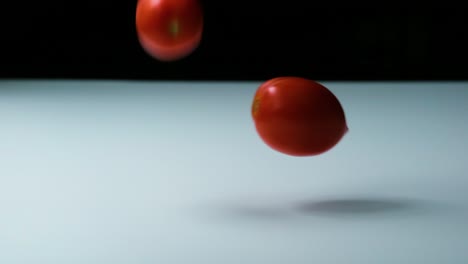 slow motion shot of tomatoes of different colours falling, bouncing and rolling onto a white surface untill they stop moving