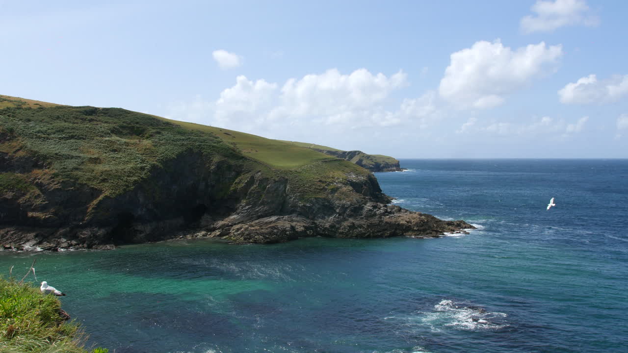 Scogliere a picco su acque turchesi cristalline lungo la costa inglese, che mostrano stratificazioni rocciose e dolci colline ricoperte di vegetazione verde