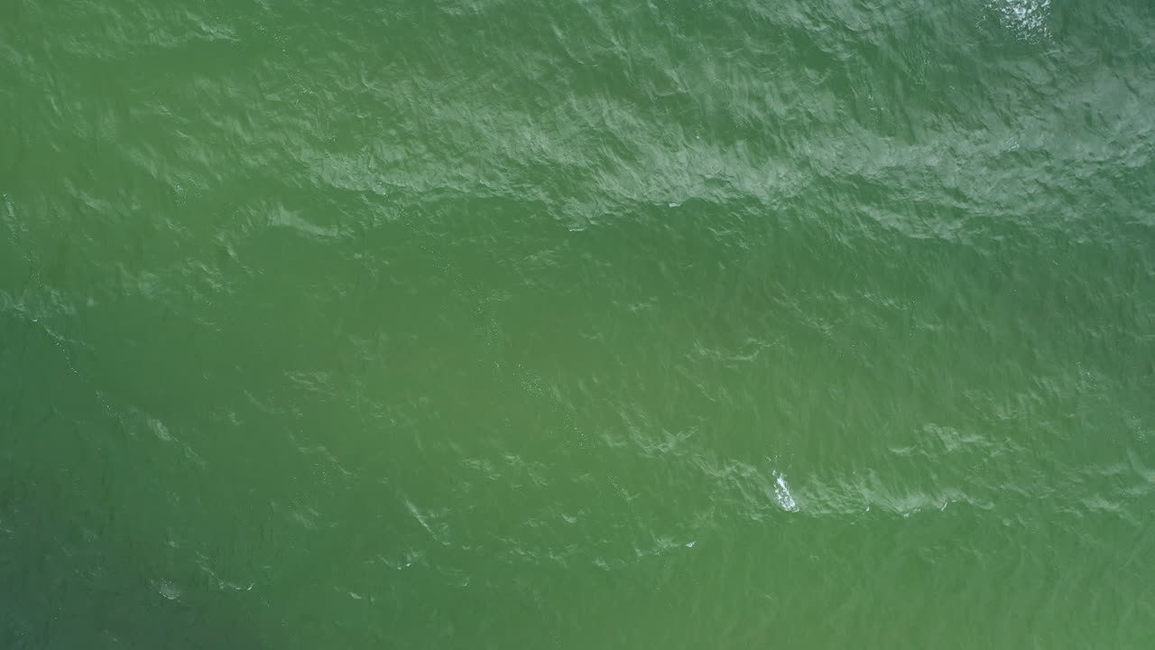 AERIAL: Rotating Shot of Waves Crashing on the Surface of Green Sea