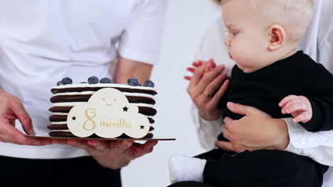 lovely blond baby is shown a chocolate cake with a sign of eight months. child wants to touch the dessert but mom holds his hand. close up.