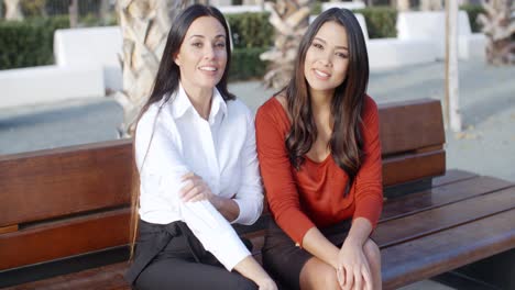 dos mujeres elegantes sentadas hablando al aire libre