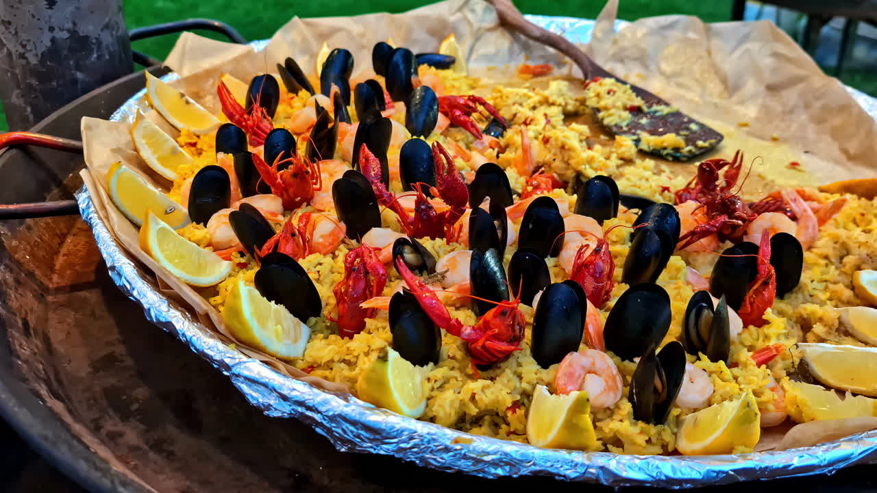 Close up of cooked vegetables and grains in black dish with colorfully arranged toppings of limes and mussels