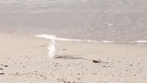 Vaso-De-Plástico-Desechado-Tumbado-En-Una-Playa-De-Arena,-Olas-En-El-Fondo,-Cuestión-Ambiental