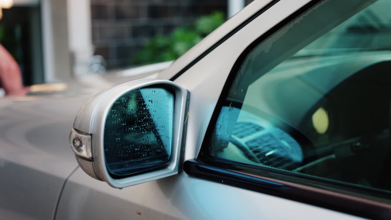 A man washing a silver car window with a cleaning brush, removing soap and dirt