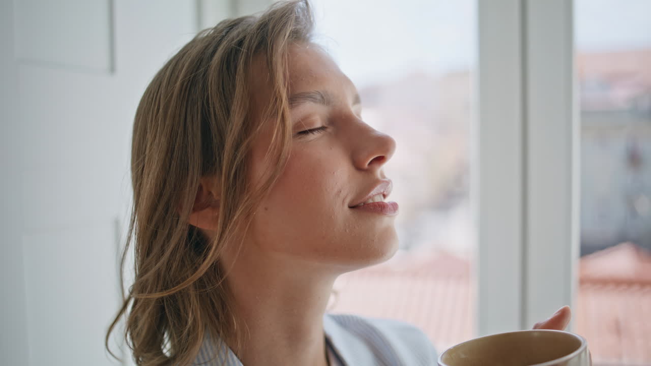 Closeup woman drinking coffee by home window. Satisfied lady tasting beverage