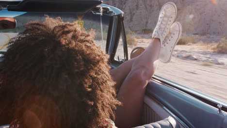 young woman with legs sticking out of moving car, back view