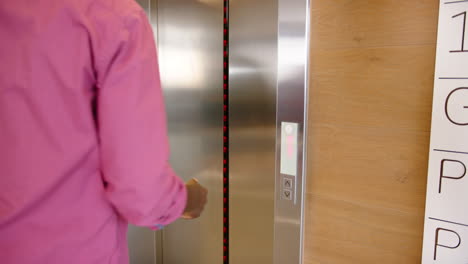 using tablet, man waiting for elevator while another man exits with laptop