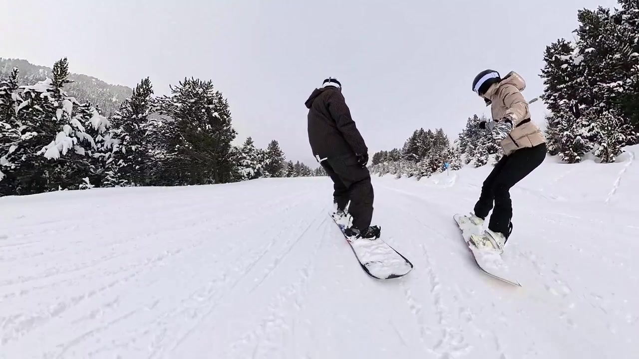 To personer, der snowboarder ned ad en sneklædt bjergskråning