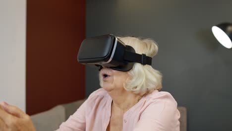 Happy-senior-woman-in-virtual-reality-headset-glasses,-trying-to-touch-something,-watching-3D-video