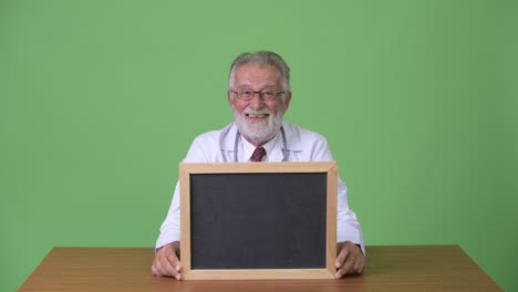 handsome senior bearded man doctor against green background